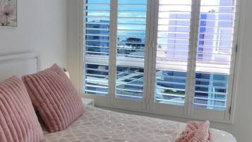 A bedroom with a patterned bedspread, two pink pillows, and a view of buildings through large windows.