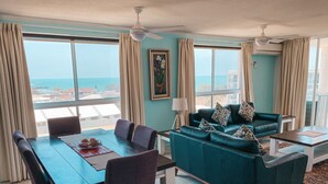 A spacious living room with a dining area, large windows, and a view of the ocean.