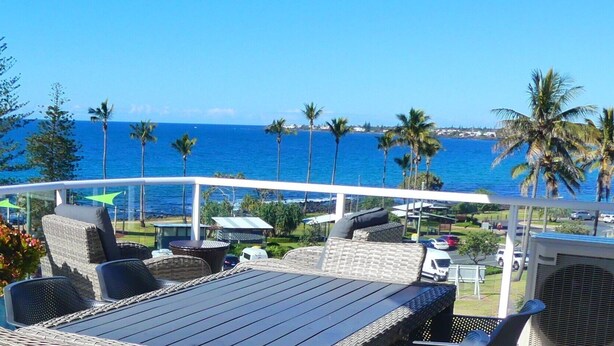 A balcony with wicker furniture, a view of the ocean, and palm trees.