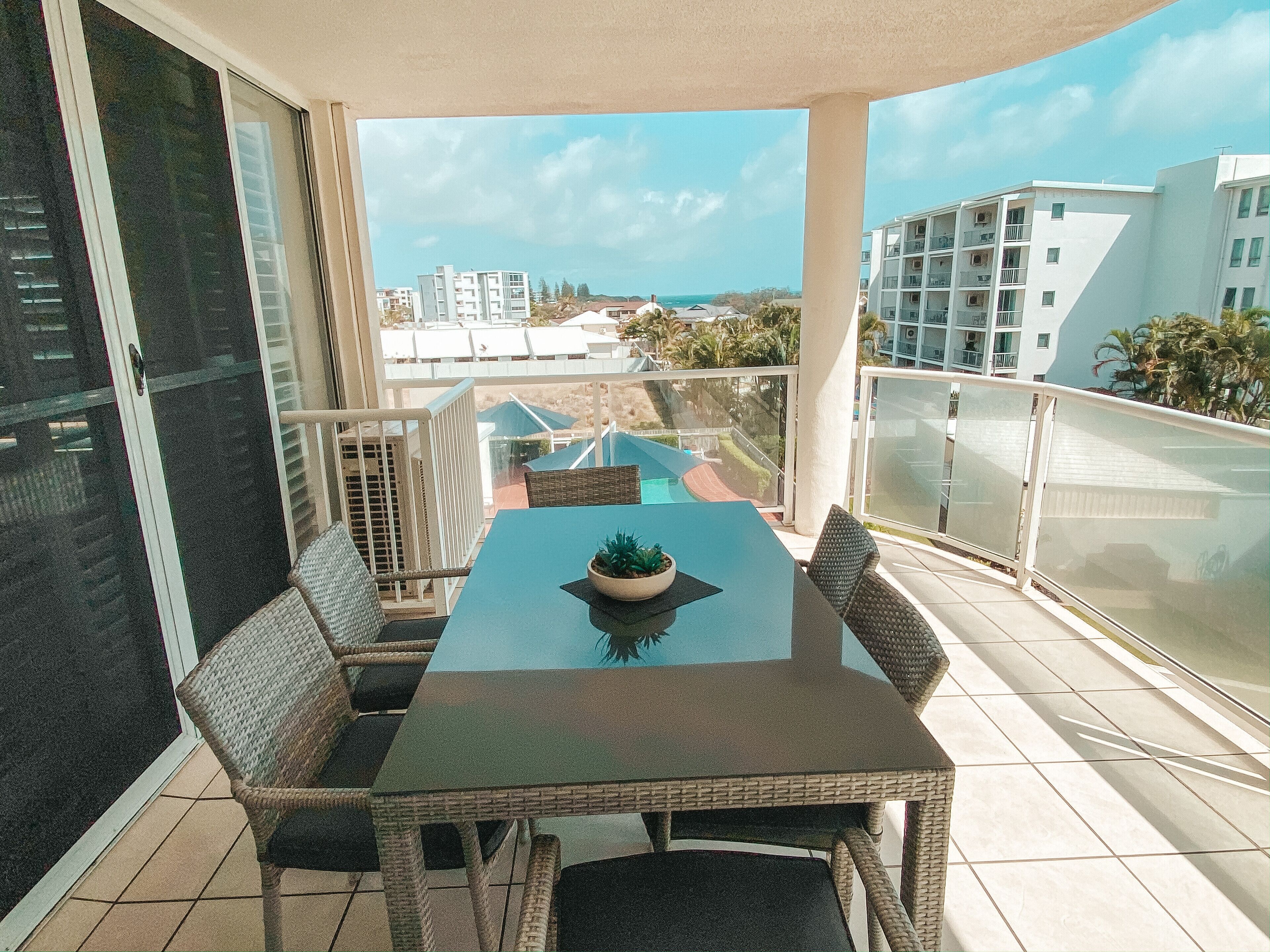 A balcony with a table and chairs, overlooking a residential area and a body of water.