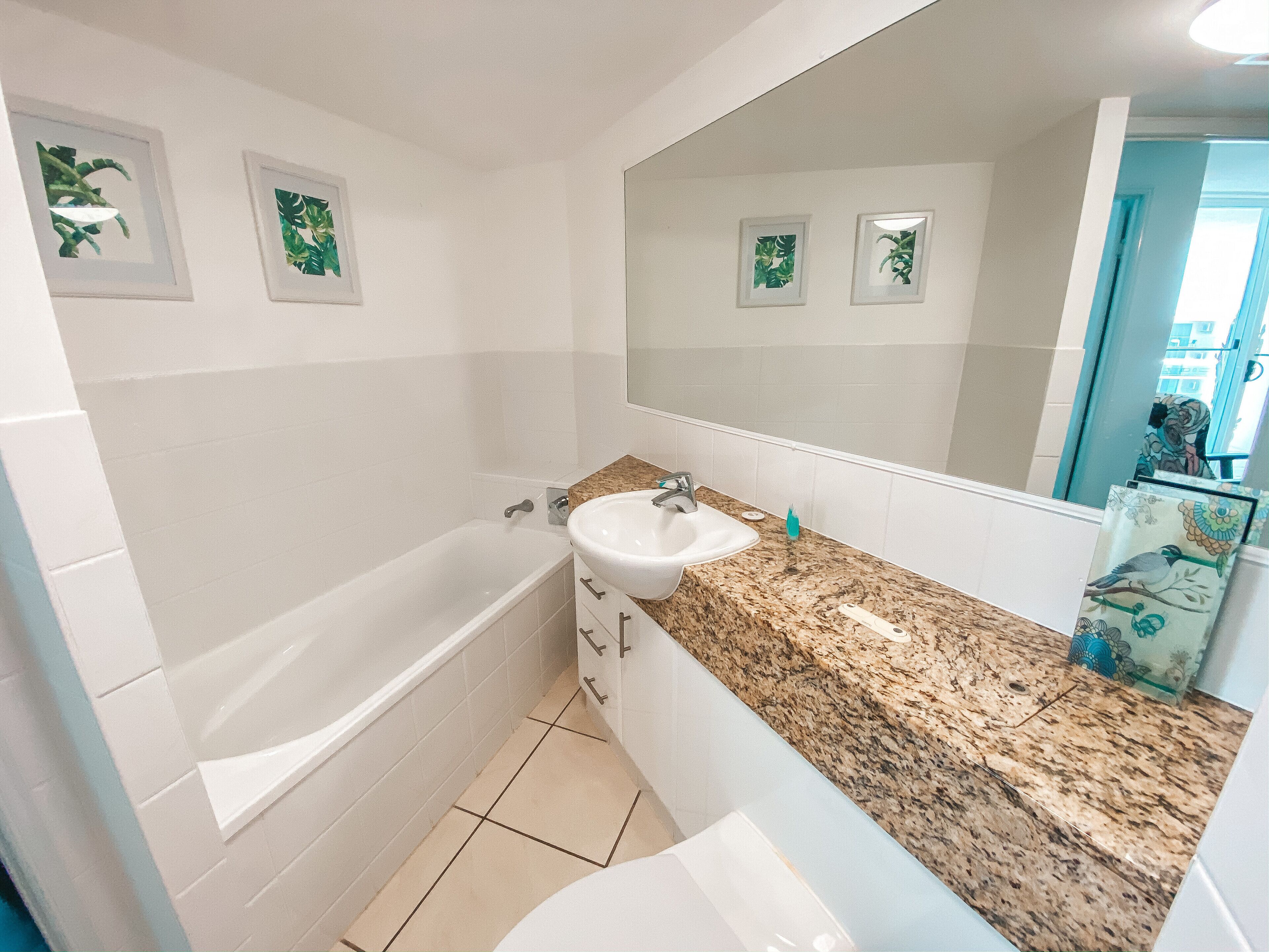 Un baño con bañera, lavabo y espejo grande. Se observan cuadros enmarcados en la pared.