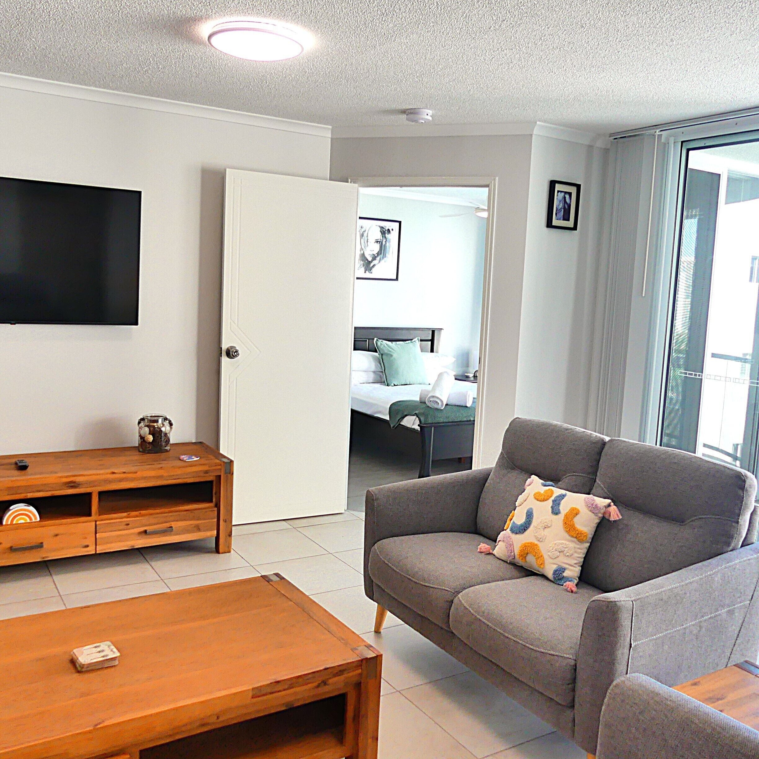 A living room with a grey sofa, a wooden coffee table, and a flat-screen TV mounted on the wall.