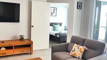 A living room with a grey sofa, a wooden coffee table, and a flat-screen TV mounted on the wall.