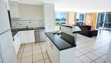 Cozinha moderna com armários brancos e bancada preta, área de jantar com sofá e mesa, e varanda com vista.