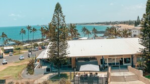 A coastal building with a flat roof, outdoor seating, and a view of the beach and ocean.