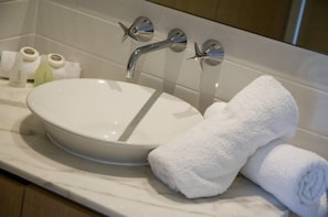 A bathroom with a white sink, two chrome faucets, and a white towel on the counter.