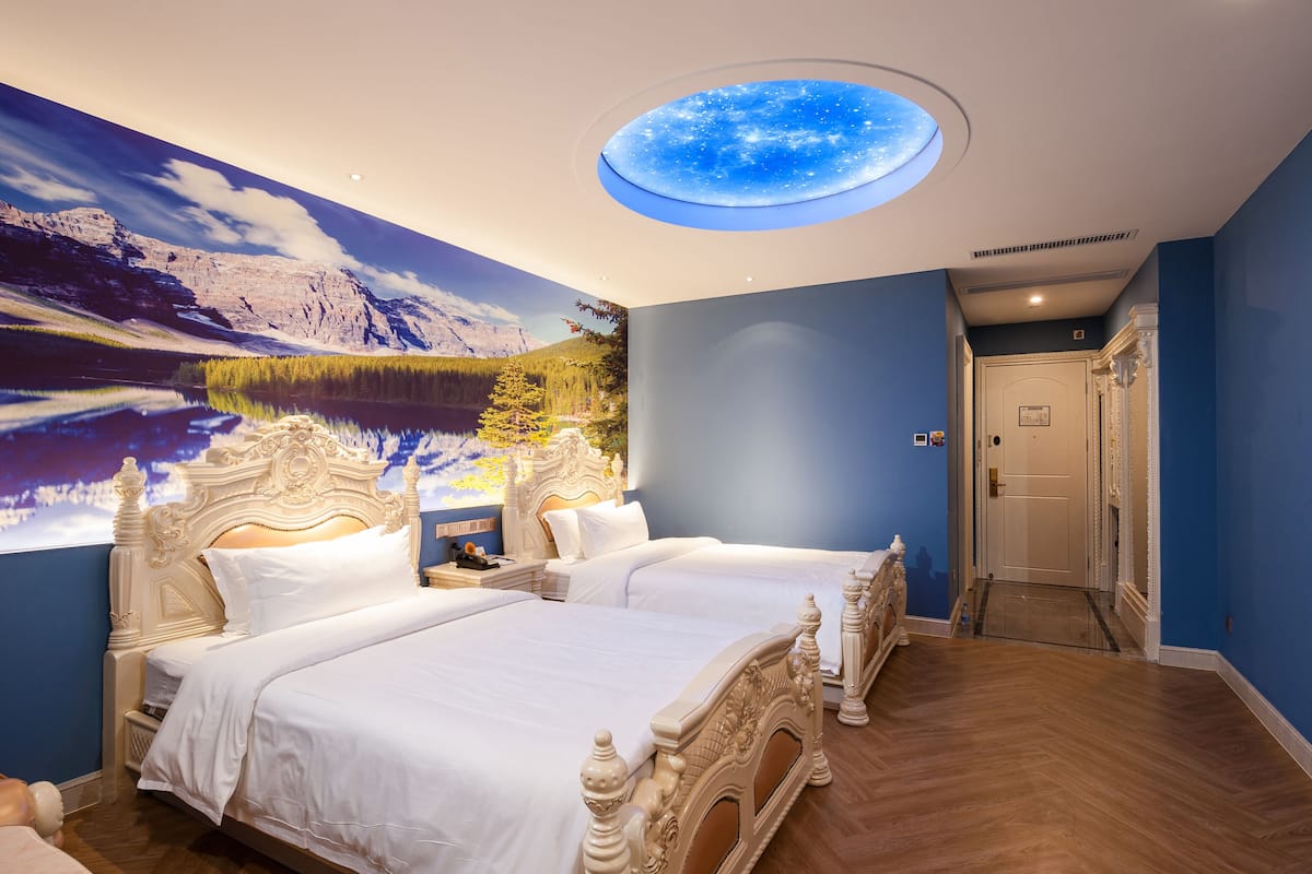 Une chambre avec deux lits, une lucarne et une fresque représentant un paysage de montagne.
