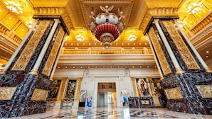 A grand lobby with marble columns, ornate chandeliers, and a large decorative ceiling.
