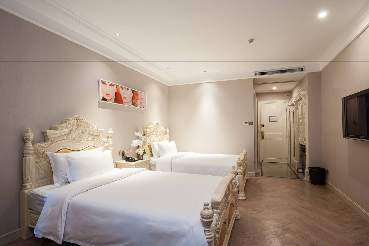 Une chambre d’hôtel avec deux lits, un téléviseur à écran plat et une porte donnant sur un couloir.