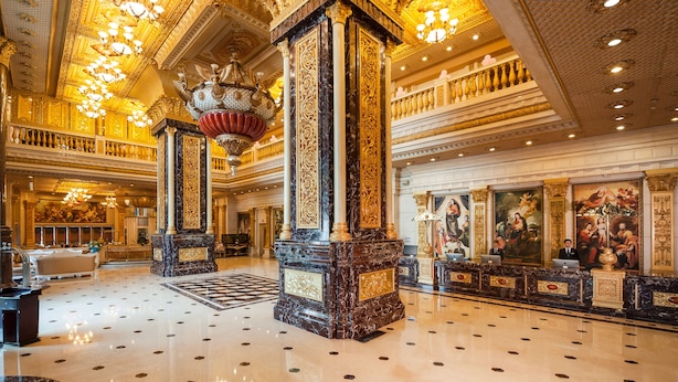 A grand lobby with marble columns, chandeliers, and classical artwork.