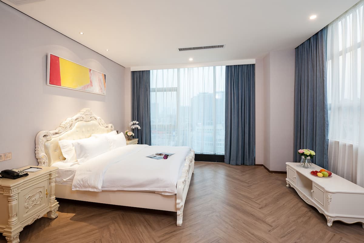 Une chambre d’hôtel moderne avec un grand lit, une table de chevet avec une lampe et une vue sur la ville grâce à de grandes fenêtres.