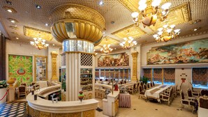 A luxurious hotel lobby with ornate chandeliers, a central column, and a large mural on the wall.
