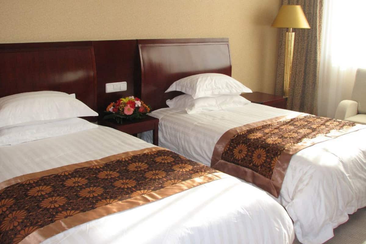 A hotel room with two beds, a nightstand with a lamp, and a floral arrangement.
