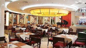Ein geräumiges Restaurant mit mehreren Tischen und Stühlen, einer zentralen Chandelüster und dekorativer Wandgestaltung.