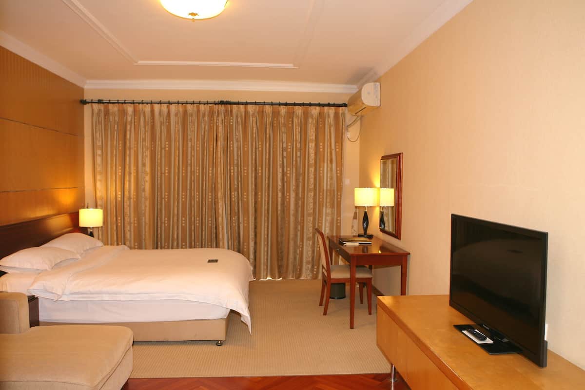A hotel room with a bed, a desk, a television, and a curtain.