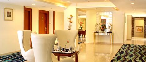 A hotel lobby with a reception desk, seating area with chairs, and a patterned carpet.