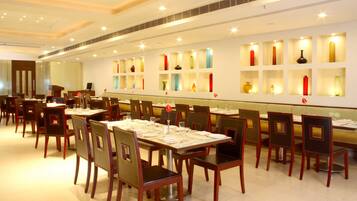 A restaurant with multiple tables and chairs, a long counter, and a wall with shelves displaying various decorative items.