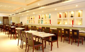 A restaurant with multiple tables and chairs, a long counter, and a wall with shelves displaying various decorative items.