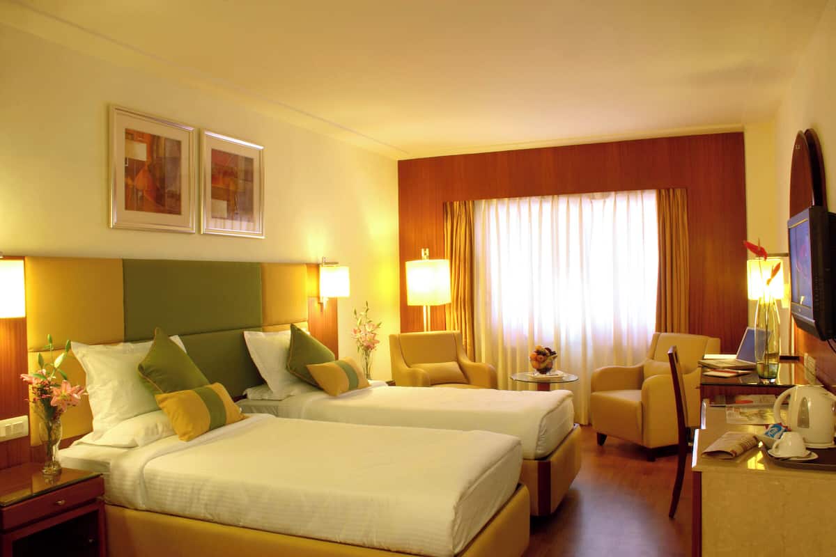 Habitación de hotel con dos camas, un escritorio con una computadora portátil, una silla y un televisor.