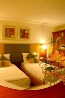 A hotel room with two beds, a nightstand, a lamp, and a vase with flowers.