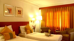 A hotel room with two beds, a desk with a laptop, a chair, and a table with a bowl of fruit.