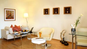 A modern living room with a sofa, armchair, coffee table, and a glass table with a laptop.