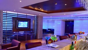 A modern bar area with a long table, bar stools, and a television screen.