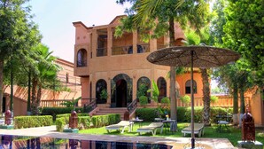 A courtyard with a swimming pool, lounge chairs, and a large umbrella. - Palais Dar Ouladna (Marrakech)