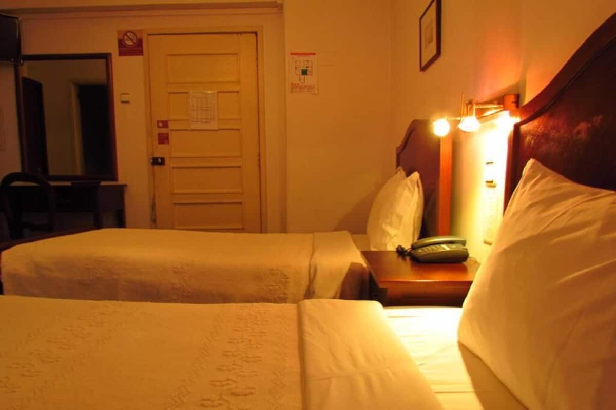 Habitación de hotel con dos camas, una mesita de noche con teléfono, un espejo y una puerta con un letrero.