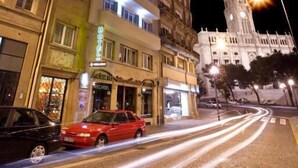 Un hotel a più piani con balconi illuminati, una torre dell'orologio ben visibile e una strada acciottolata.