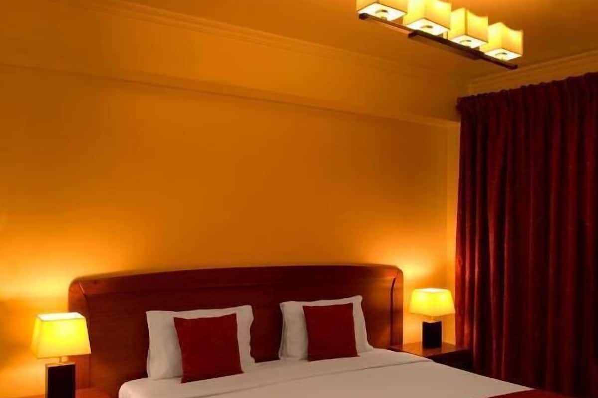 Habitación de hotel con una cama grande, dos lámparas de noche, una computadora portátil sobre la cama y una cortina roja.