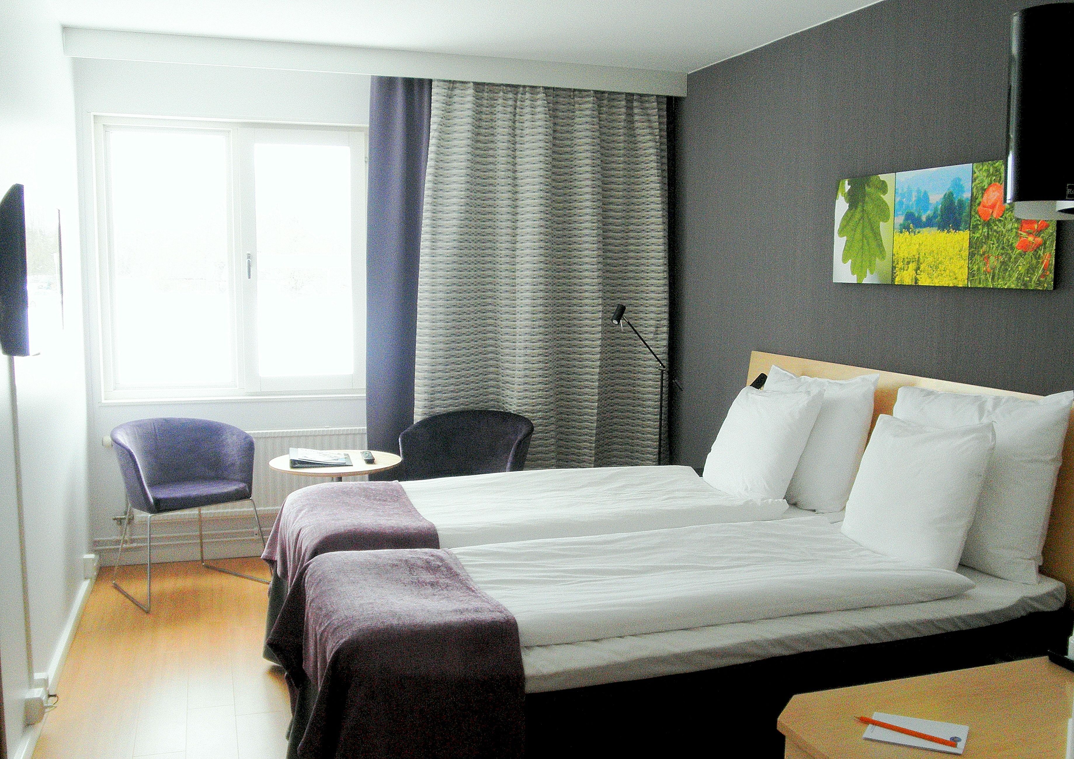 Habitación de hotel con una cama grande, dos sillas, una mesita y un cuadro en la pared.