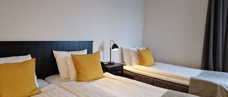 Una habitación de hotel con dos camas, cada una con cabecera, una mesita de noche con lámpara y ventana con cortinas.