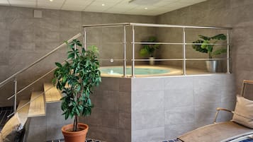 Un área de piscina interior moderna con suelo de baldosas azules, una zona de estar con una silla y una escalera con barandilla.