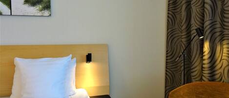 A hotel room with a bed, a nightstand, a lamp, a chair, and a patterned curtain.