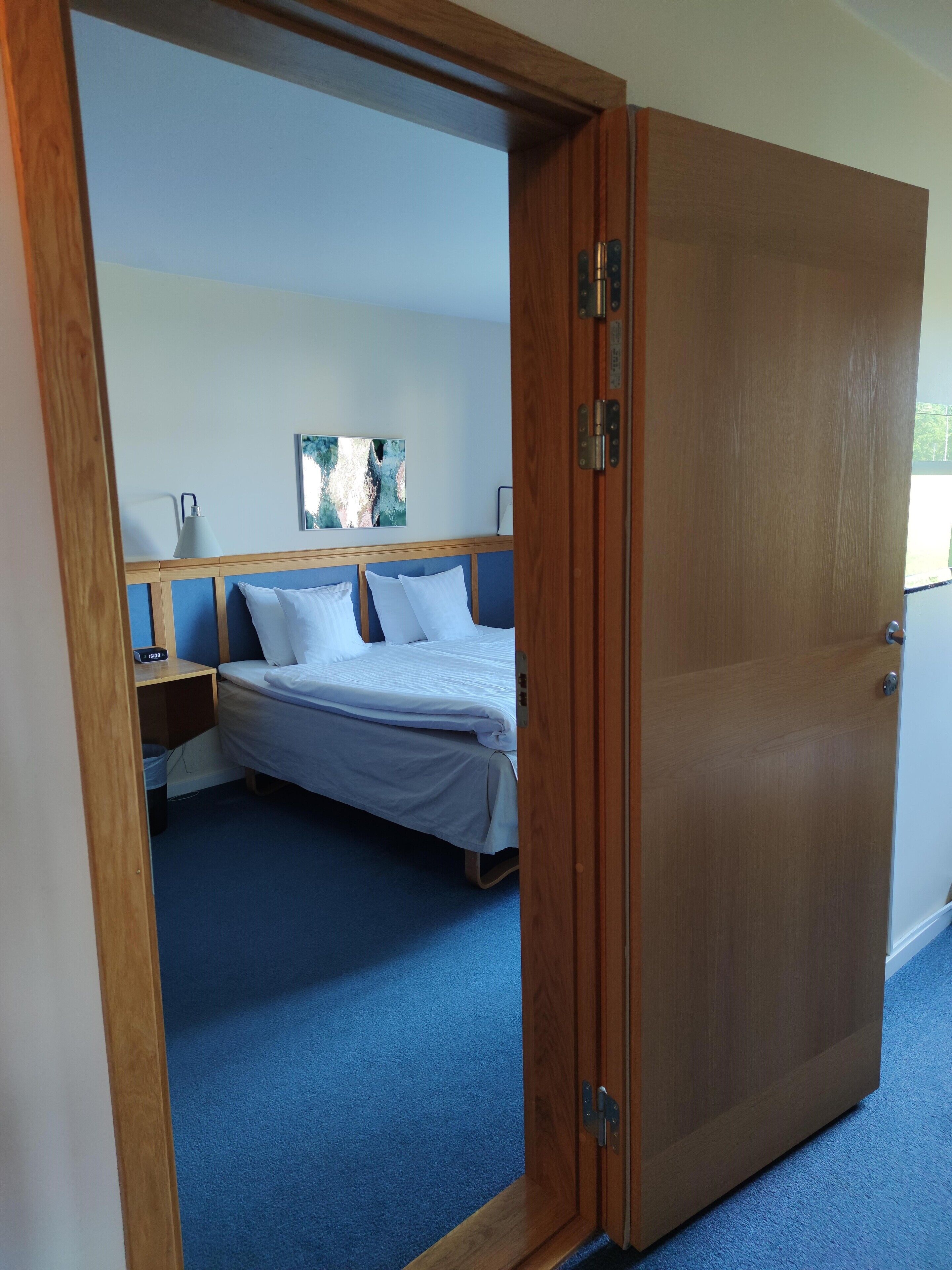 Ein Hotelzimmer mit Bett, Nachttisch, Lampe und einem Gemälde an der Wand.