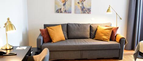 A modern living room with a grey sofa, yellow and brown cushions, a black coffee table, a gold desk lamp, and two wall-mounted paintings of deer.
