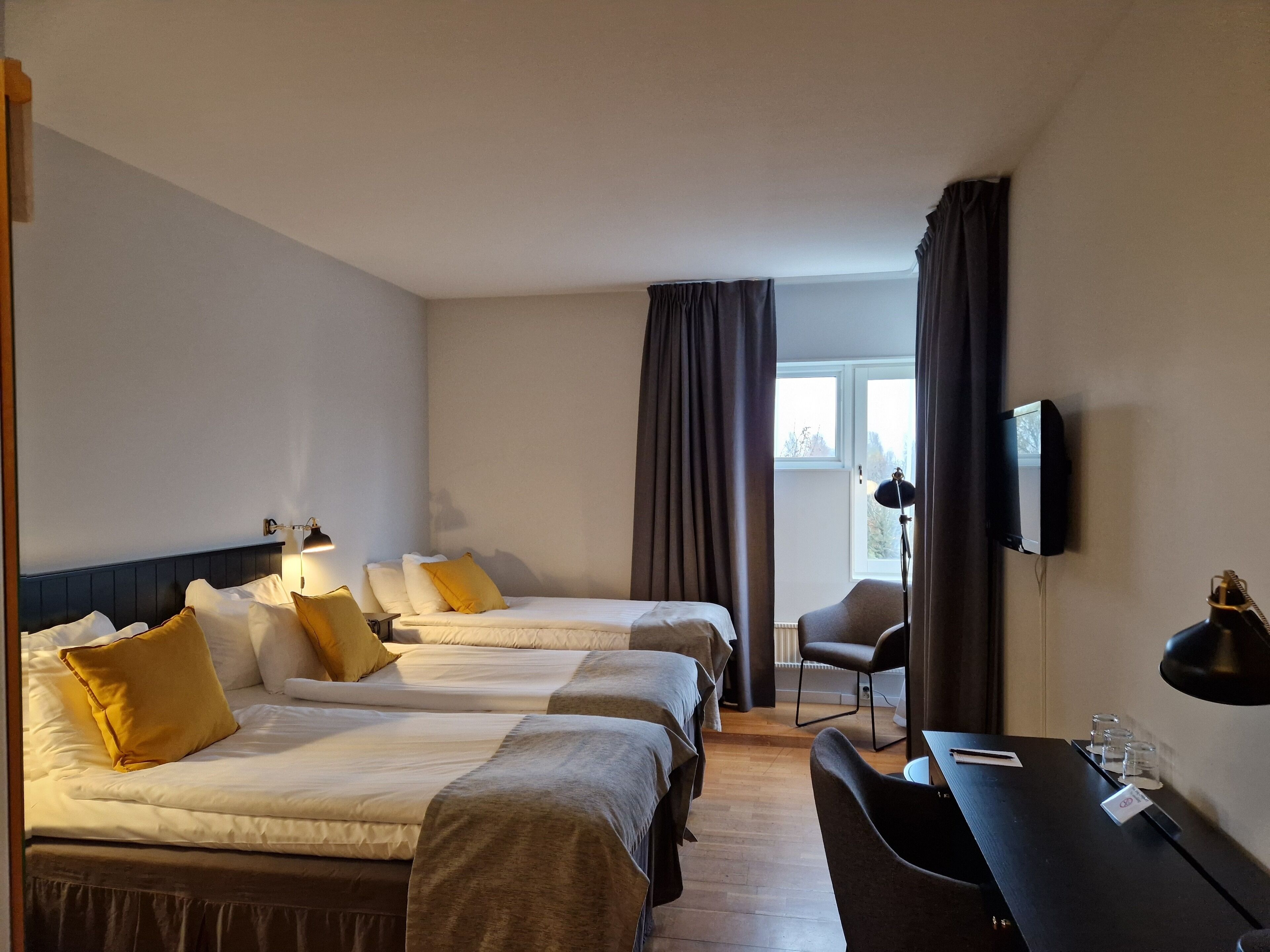 Een hotelkamer met twee bedden, een bureau, een stoel, een televisie en een raam met gordijnen.