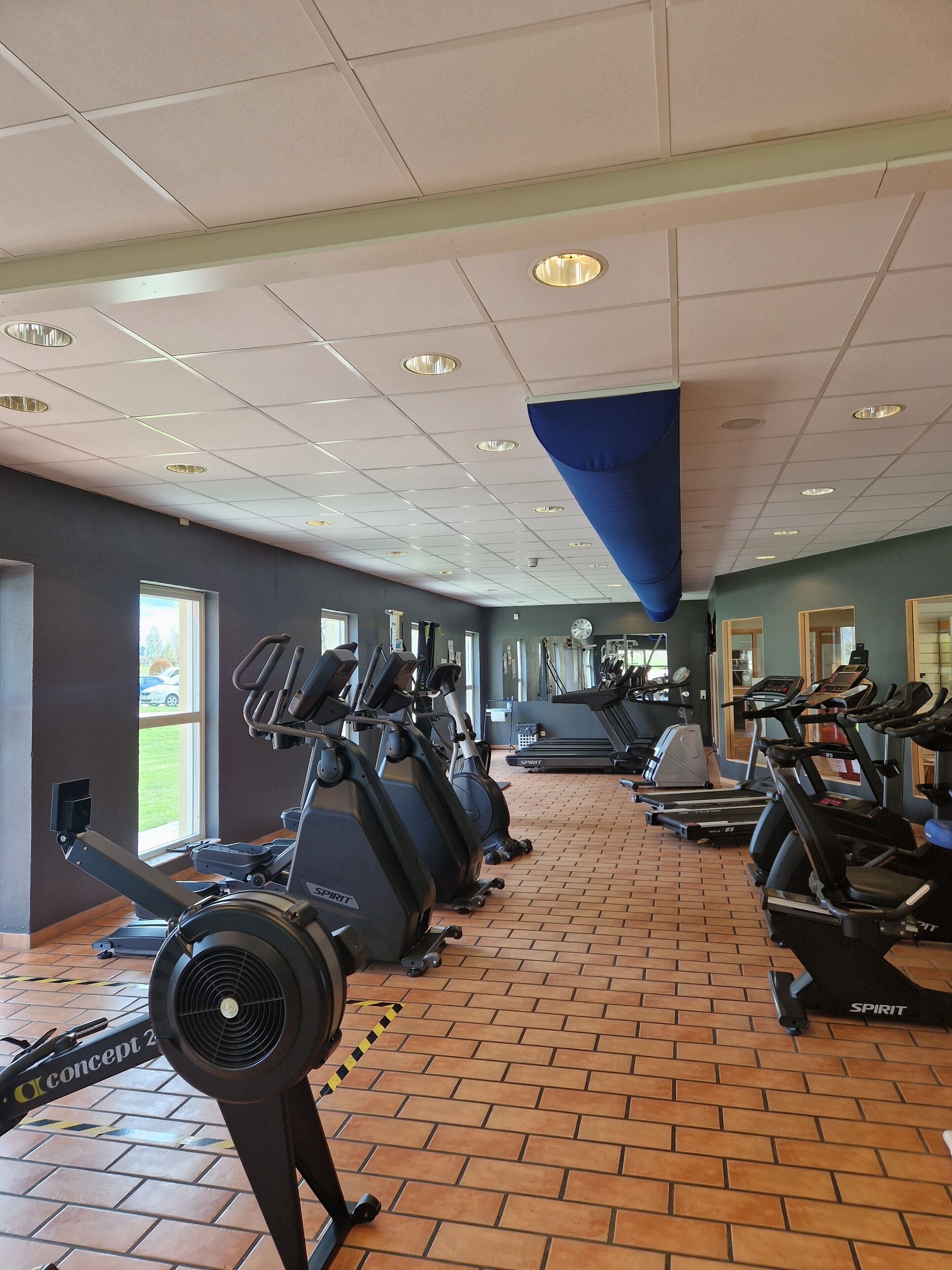 Ett gym med flera löpband, motionscyklar och ett golv som är belagt med tegelplattor.