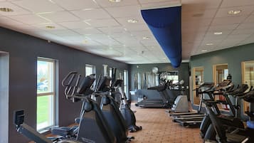 Ett gym med flera löpband, motionscyklar och ett golv som är belagt med tegelplattor.