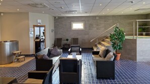 Un hall d’entrée moderne comprenant un comptoir d’accueil, un espace détente avec des canapés et des fauteuils, un escalier et une plante en pot.