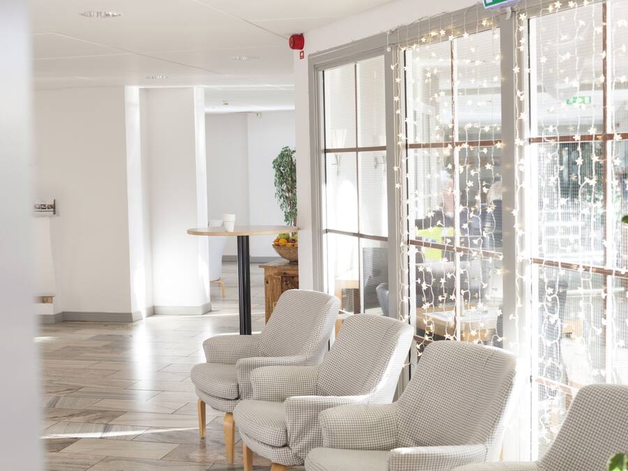 A modern hotel lobby with checkered armchairs, a wooden table with a fruit bowl, and large windows with decorative string lights.