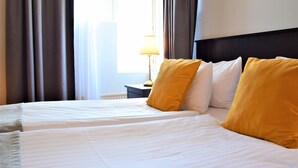 Une chambre d’hôtel avec un grand lit, deux oreillers, une table de chevet avec une lampe et une fenêtre avec des rideaux.