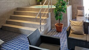 Un espace de détente avec un escalier menant à un bain à remous, une plante en pot et un coin salon comprenant une chaise et des coussins.