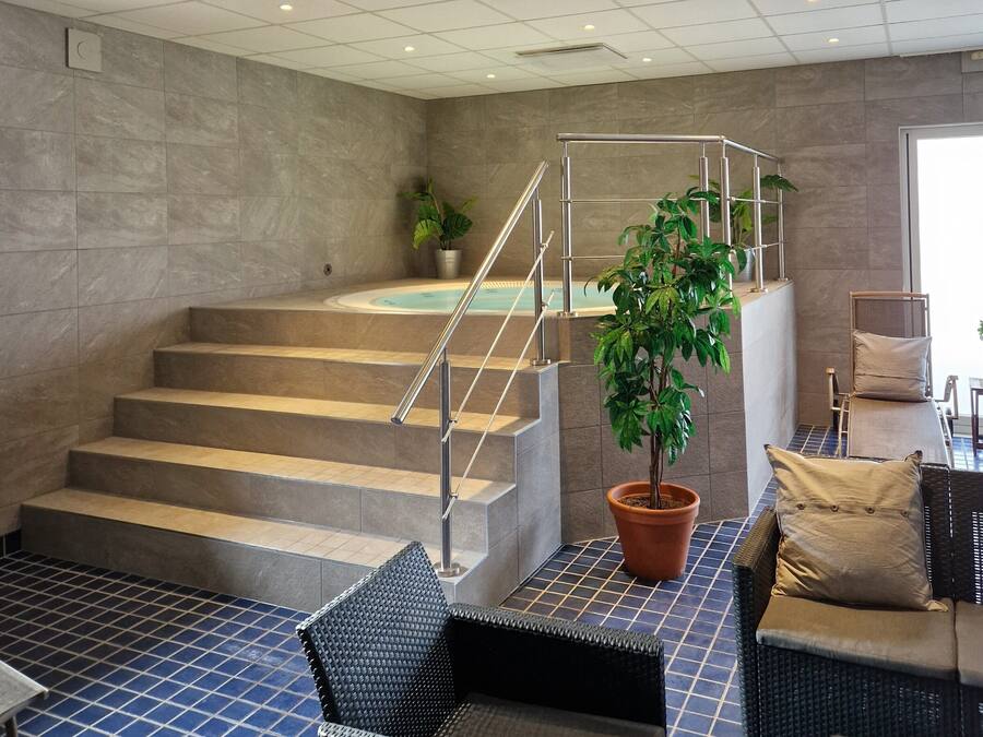 A spa area with a staircase leading to a hot tub, a potted plant, and a seating area with a chair and cushions.