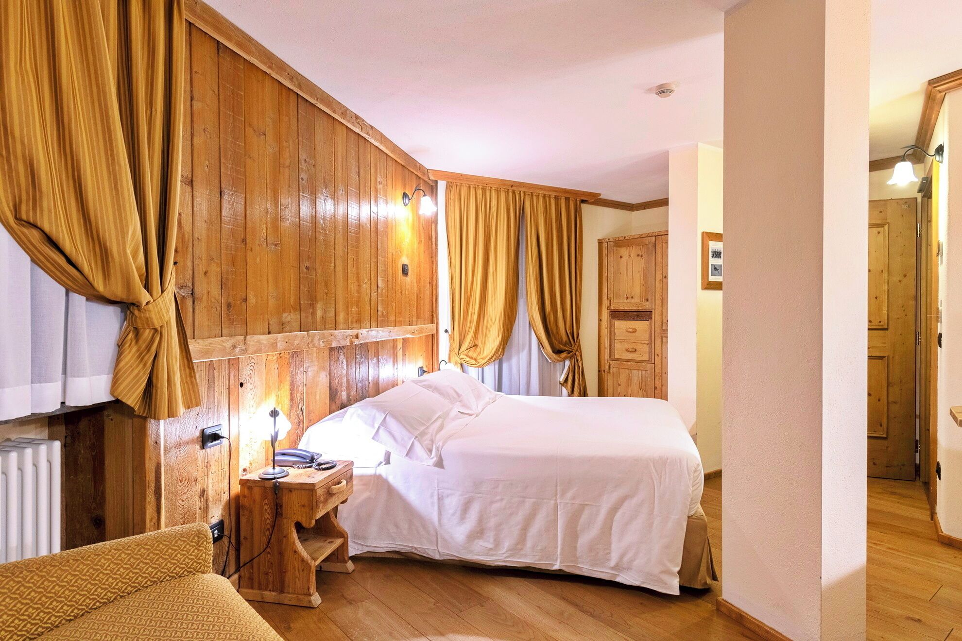 Un dormitorio con cabecera de madera, una cama con ropa de cama blanca, una mesita de noche de madera con una lámpara y un armario de madera.