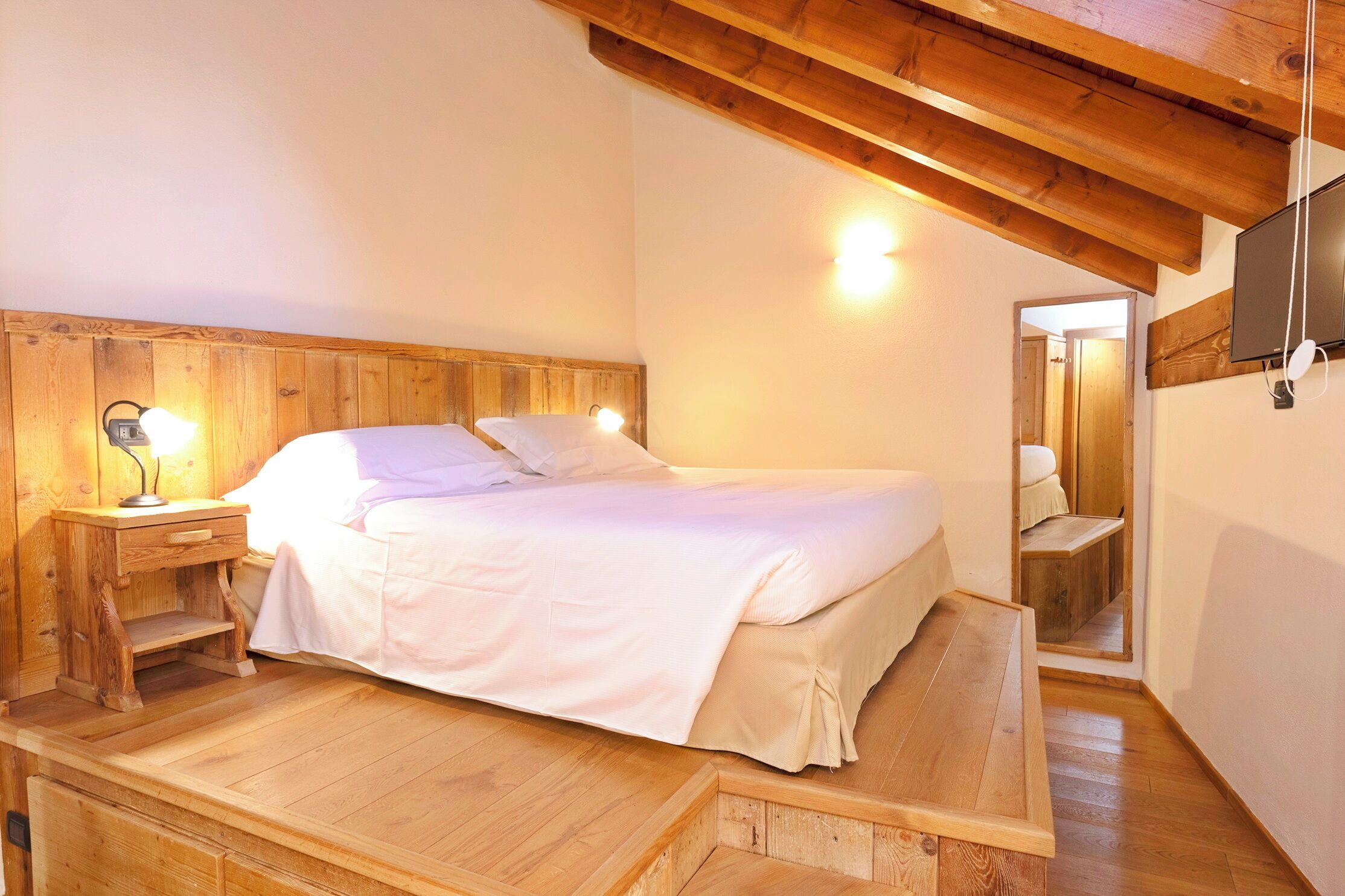 A wooden-framed bedroom with a bed, bedside tables, and a TV mounted on the wall.