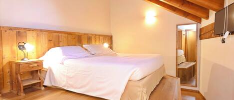 A wooden-framed bedroom with a bed, bedside tables, and a TV mounted on the wall.