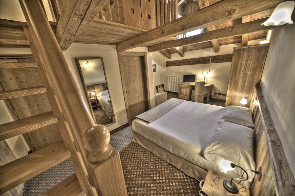 A wooden-floored bedroom with a bed, bedside lamps, and a mirror.