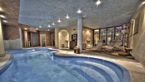 An indoor swimming pool with a stone wall, a lounge area with chairs, and a ceiling with a starry design. - Le Miramonti Hotel & Wellness (La Thuile)